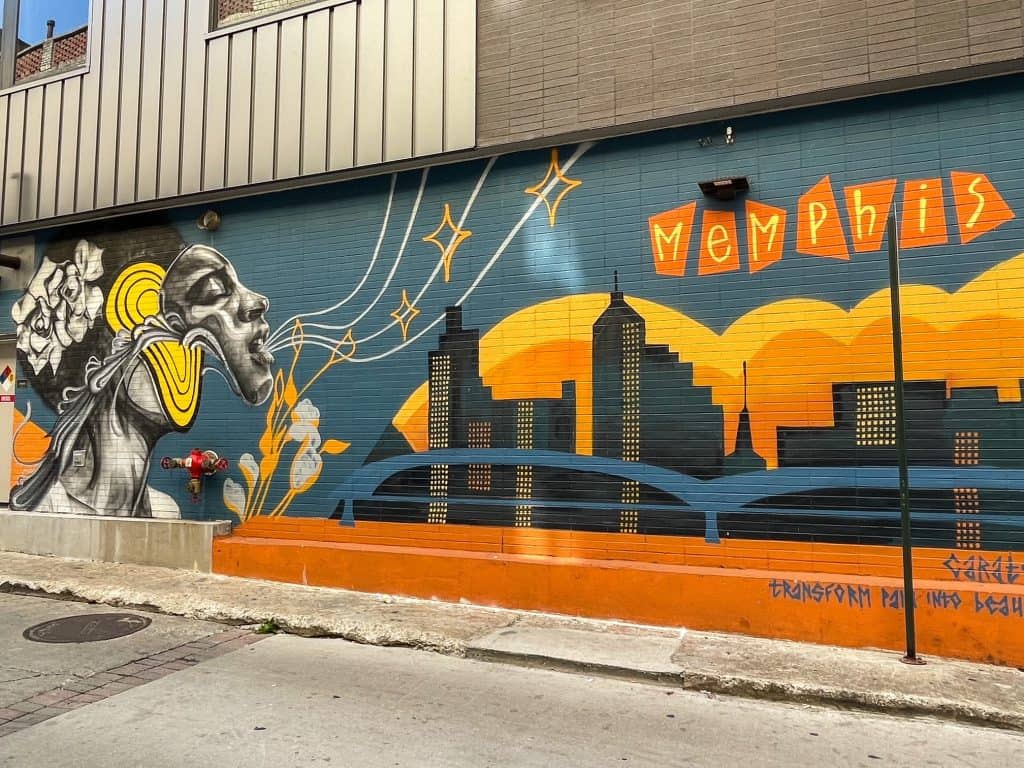 A art mural in the alleyway of Rendezvous with a person singing over the skyline of Memphis.