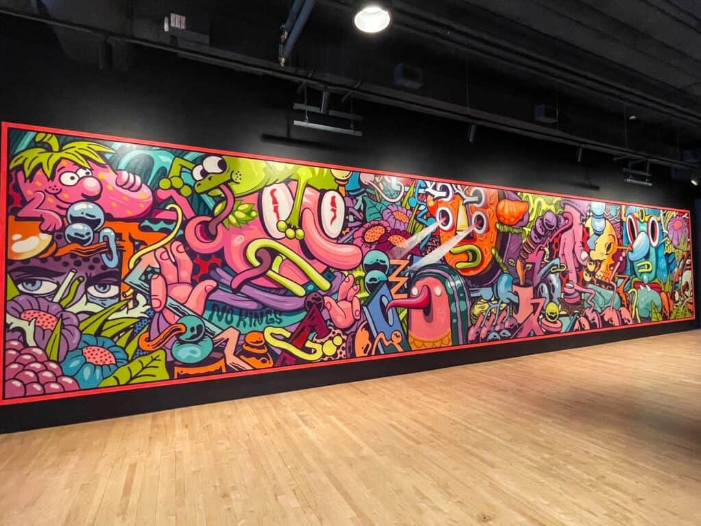 A very long art mural stretching the entire wall filled with abstract and colorful cartoon like characters in the art gallery at Crosstown.
