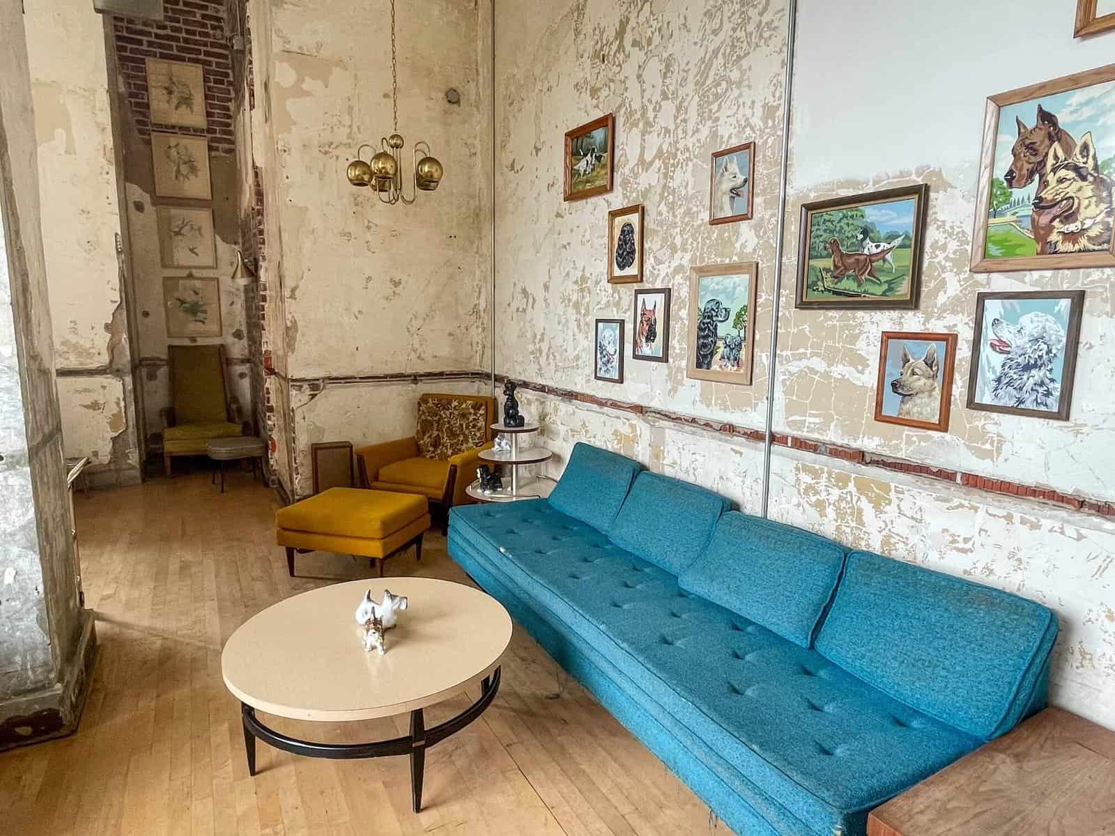 A bright blue couch, vintage style chair, decor, and artwork of dogs in the cool hidden bar in Memphis.