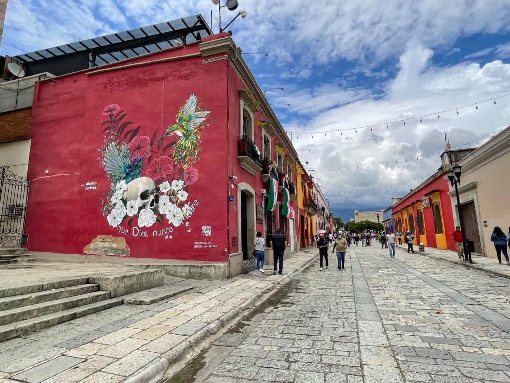 Walking down Calle Alacala with bright colored buildings and a huge art mural with a skull and flowers on it in Oaxaca City.