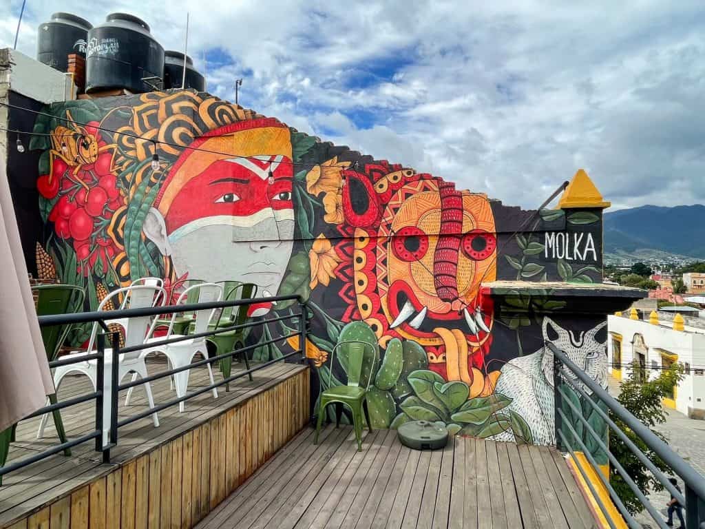 A bright red, orange, yellow, white and black art mural on a rooftop restaurant with indigenous depictions.