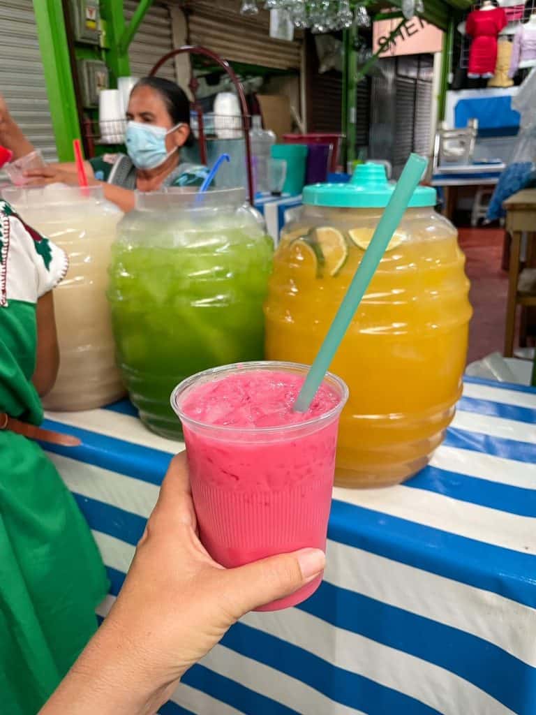 Drinking a fresh fruit water that is pink with a batch of lime and orange behind it at the Central Abastos Market in Oaxaca City, Mexico.