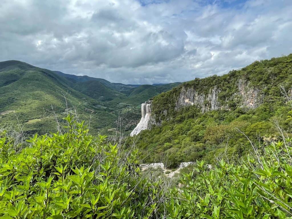 Looking out a large petrified waterfall among super green and lush vegetation across the canyon at Hierve el Agua.