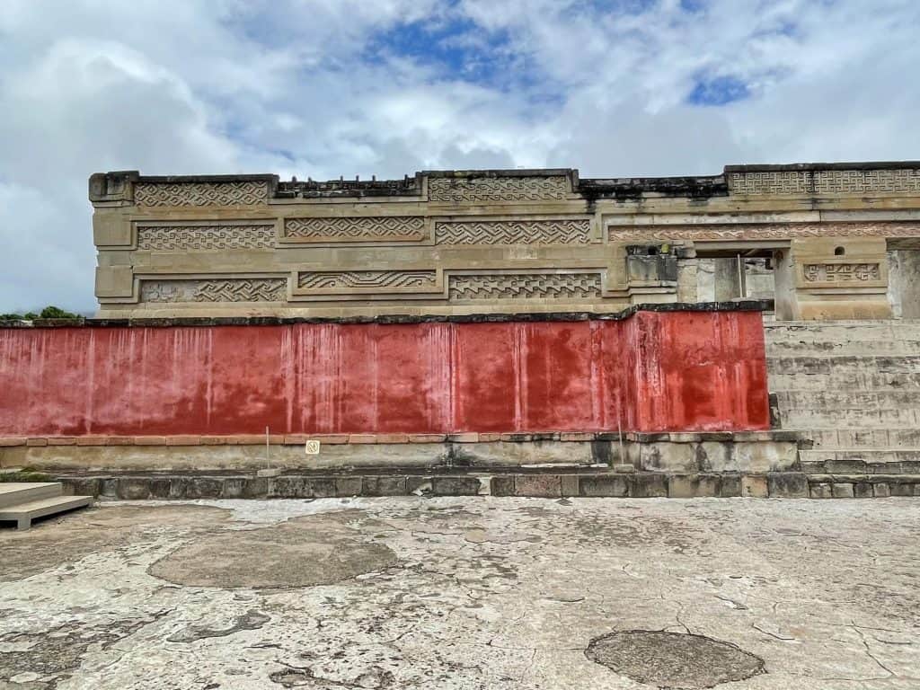 A pyramid like structure with dark red panels on the walls with detailed carvings in the stone at Mitla outside of Oaxaca City, Mexico.