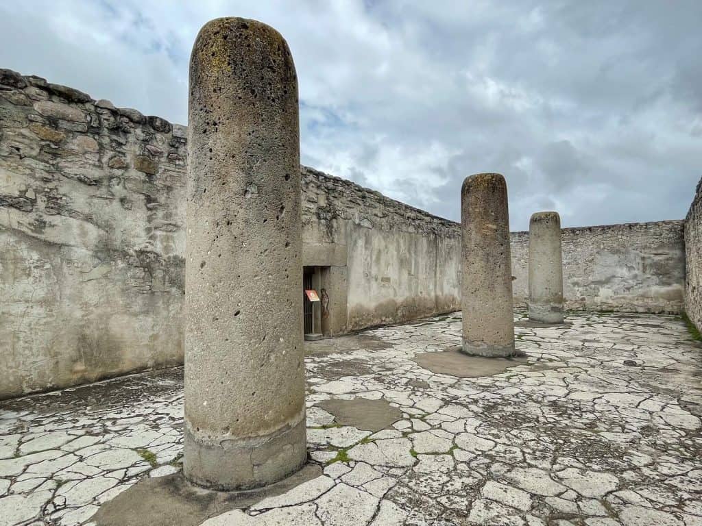 Three massive stone pillars spread apart in a courtyard at the ruins of Mitla outside of Oaxaca City.