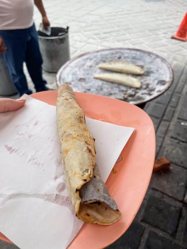 A eating a taco that is rolled and looks more like a large taquito from a street vendor in Oaxaca City.