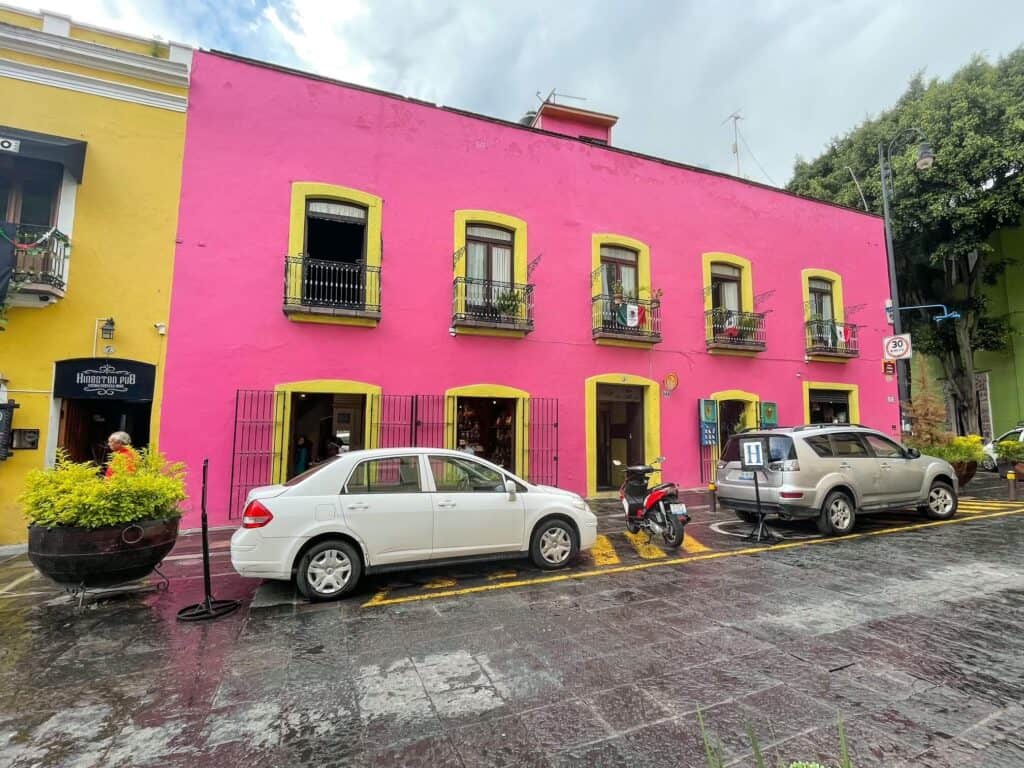 A bright colored pink building with yellow window trim along Alley of the Frogs in the heart of Puebla, Mexico.