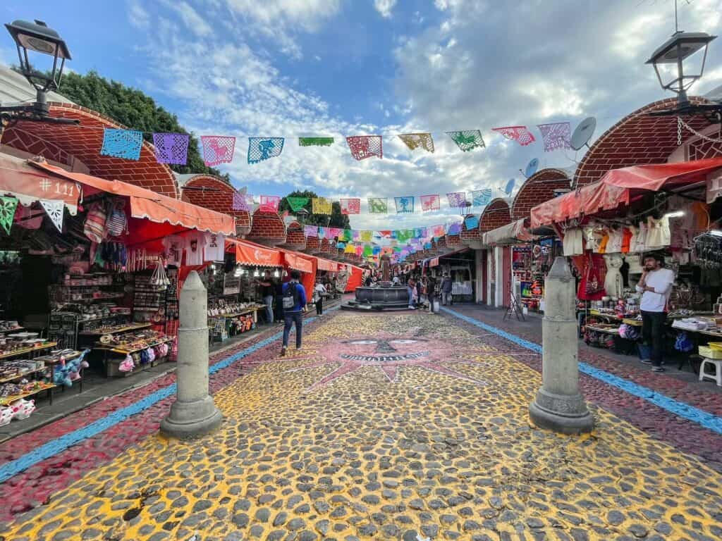 Walking through the vibrant outdoor Parian market lined with vendors, painted walkway, and hanging flags.