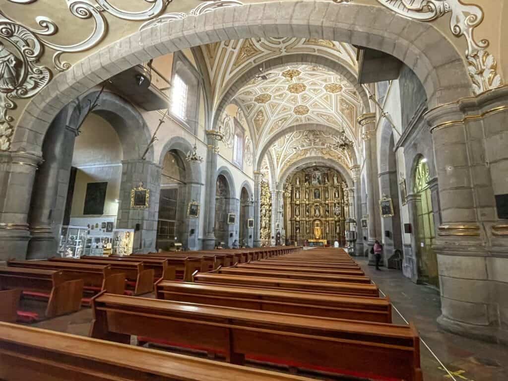The main area of Templo de Santo Domingo when you first walk in with rows of pews, a grand ceiling, and beautiful alter up front in Puebla.