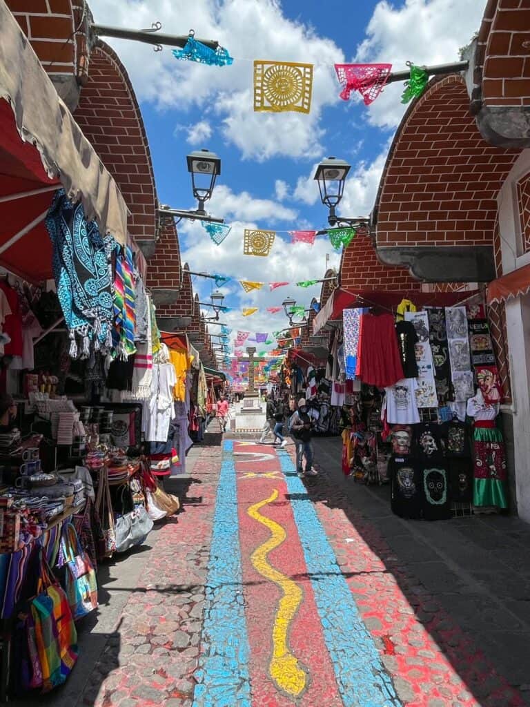 The ground is painted with several colors in the outdoor Parian market with vendors selling items on each side.
