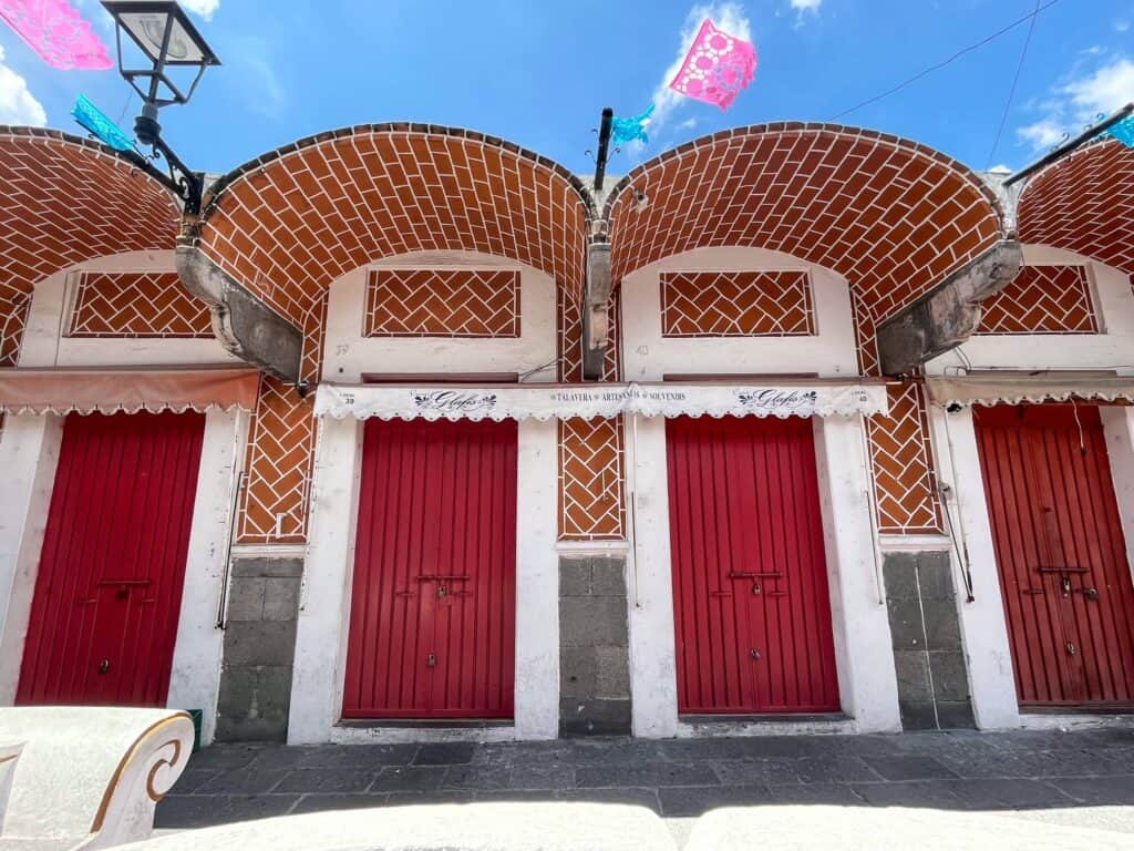 Beautiful series of bright red doors trimmed in white and decorative awnings that are tiny art and shop studios in the El Parian market in Puebla City, Mexico.