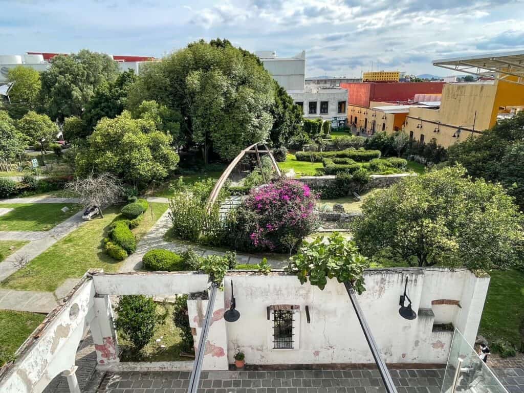 Looking down on Jardin de San Francisco from my hotel balcony with views of trees, ruins, sculptures, walkways, and benches to sit.