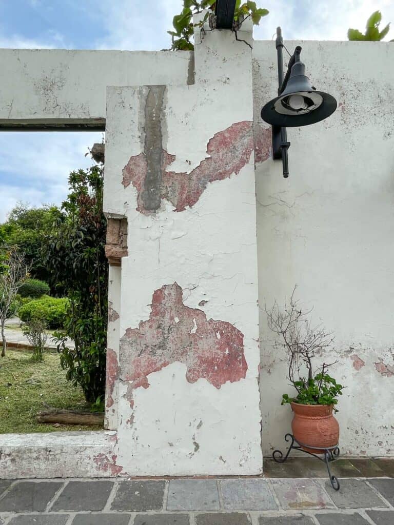 A close up view of partial ruins or walls painted white with paint peeling off, planters, and a light which are pretty and great for photo backdrop. 