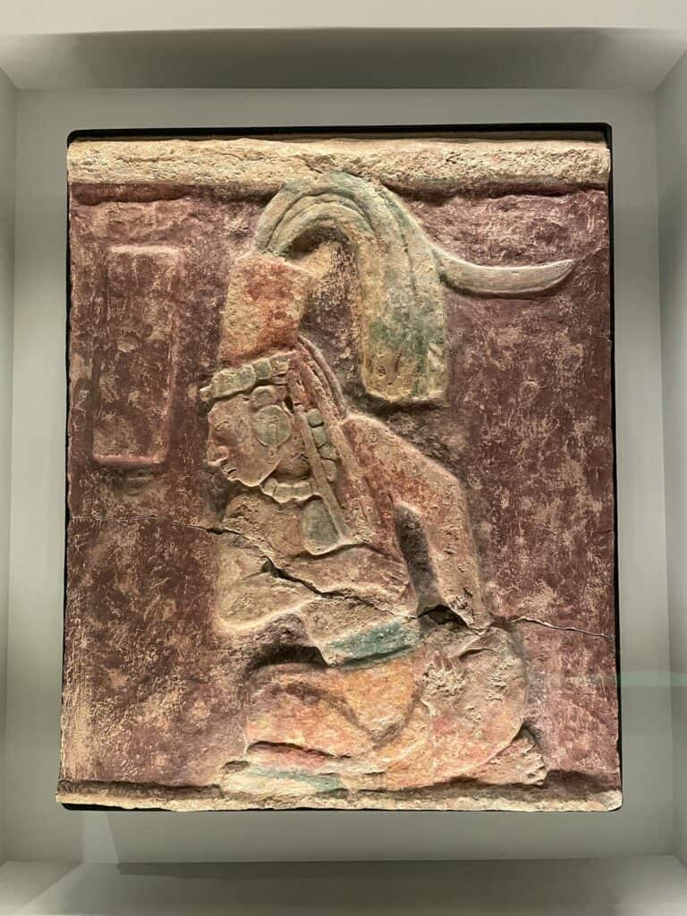 A stone square slab with a carving of a warrior and dyed in colors of red and green.
