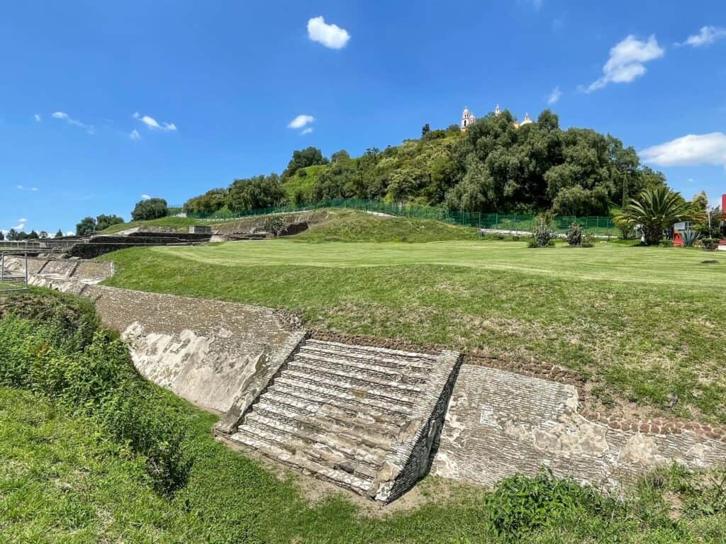 Walking around the base of the Cholula pyramid with most of it covered up with dirt, grass, and trees.