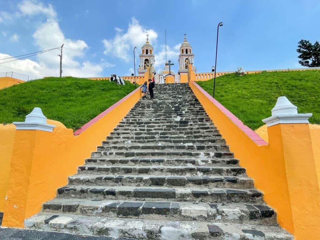 Walking up the final steps to the church at the top of the Cholula pyramid with a bright yellow color.
