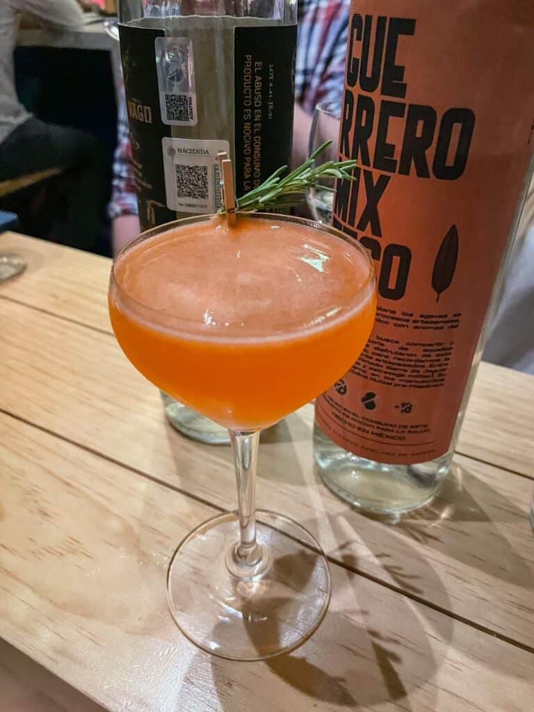 A delicious cocktail made with mezcal, fresh juices, and herbs that has a orange color at a mezcal bar in San Miguel de Allende.