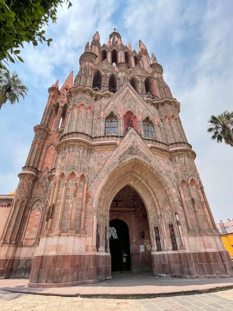 Standing facing the front of the pink La Parroquia de San Miguel Arcangel church and admiring the breathtaking architecture and beauty of it.