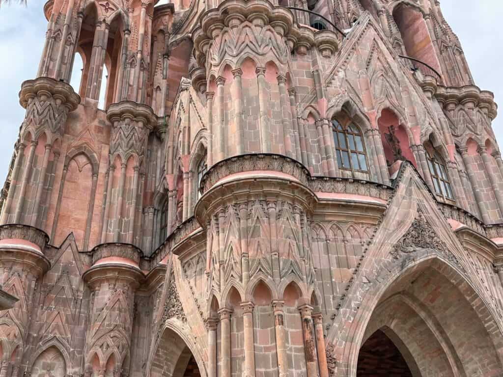 A close up of one section of the exterior to the pink La Parroquia de San Miguel Arcangel church to view the exquisite carvings and architecture and various shades of pink in the stone.