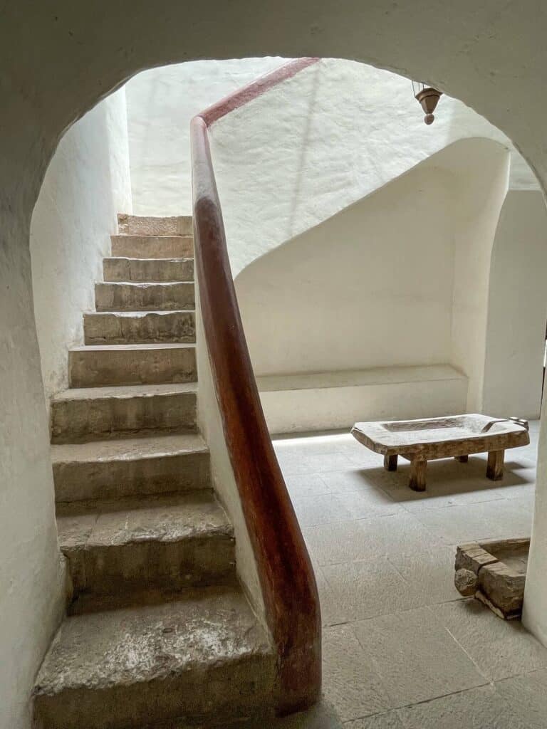 Walking up a curved staircase with stark white walls throughout the interior of the former home of Ignacio Allende.