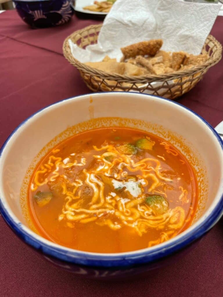 A bowl of delicious soup with red broth, yellow cheese, and crema on a food tour in San Miguel de Allende. 