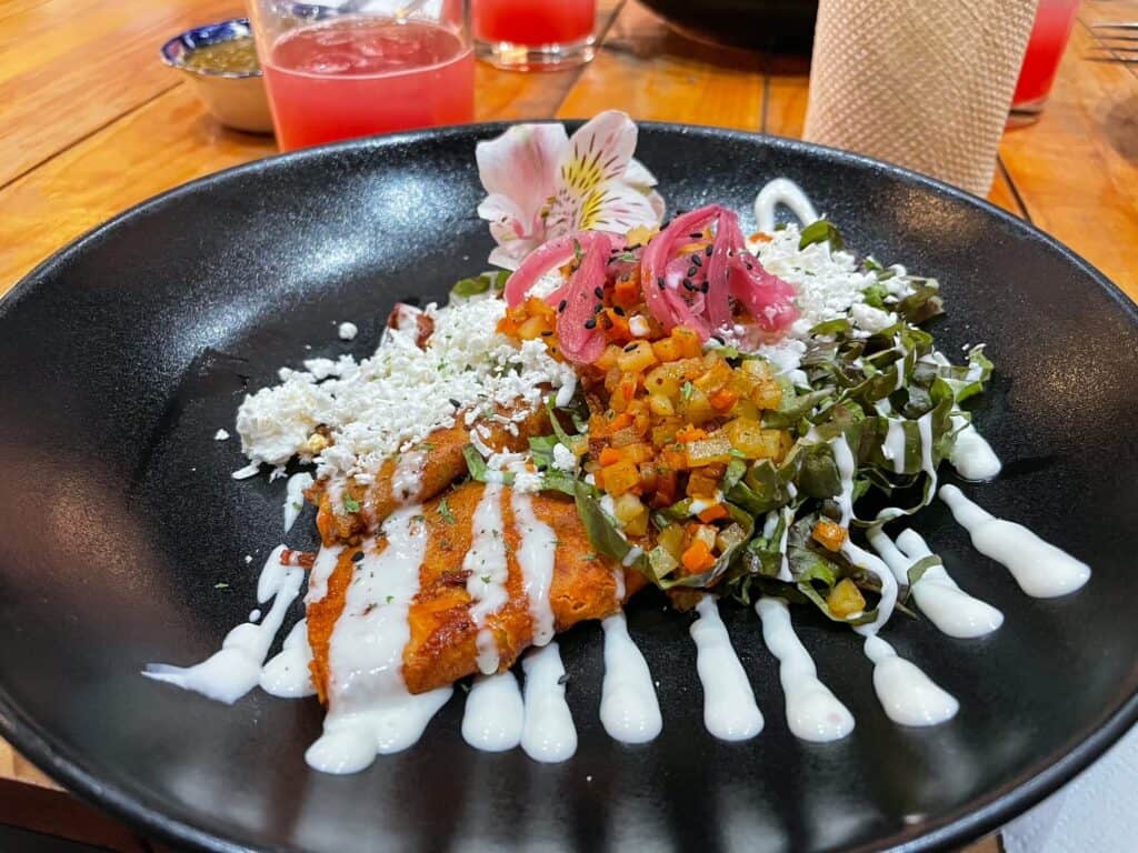 A plate with two enchiladas on it known as Miners enchiladas covered in chopped veggies, caramelized onions, crema and cheese on a food tour in San Miguel de Allende.