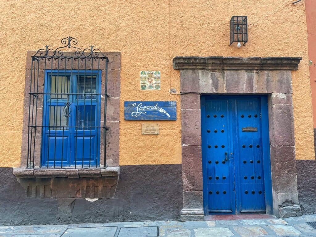 The outside of Lavanda with its bright blue door and window against a tan colored building in the center of San Miguel de Allende, Mexico.