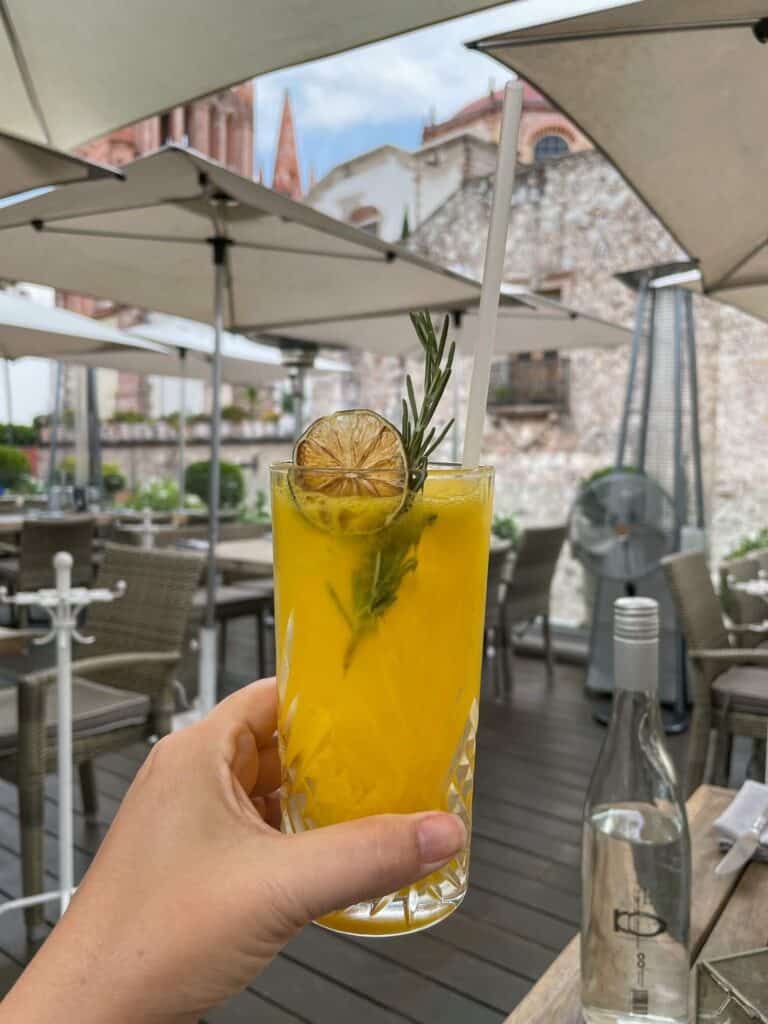Holding a mango and mezcal cocktail on the rooftop bat at Quince and a front row view of the church towers of La Parroquia.