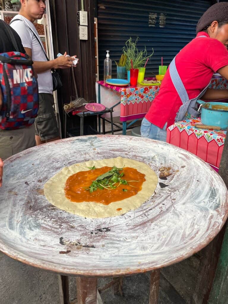 A large tortilla cooking on a huge comal with yellow mole sauce on the tortillas, herbs, and squash blossoms in Oaxaca, Mexico.