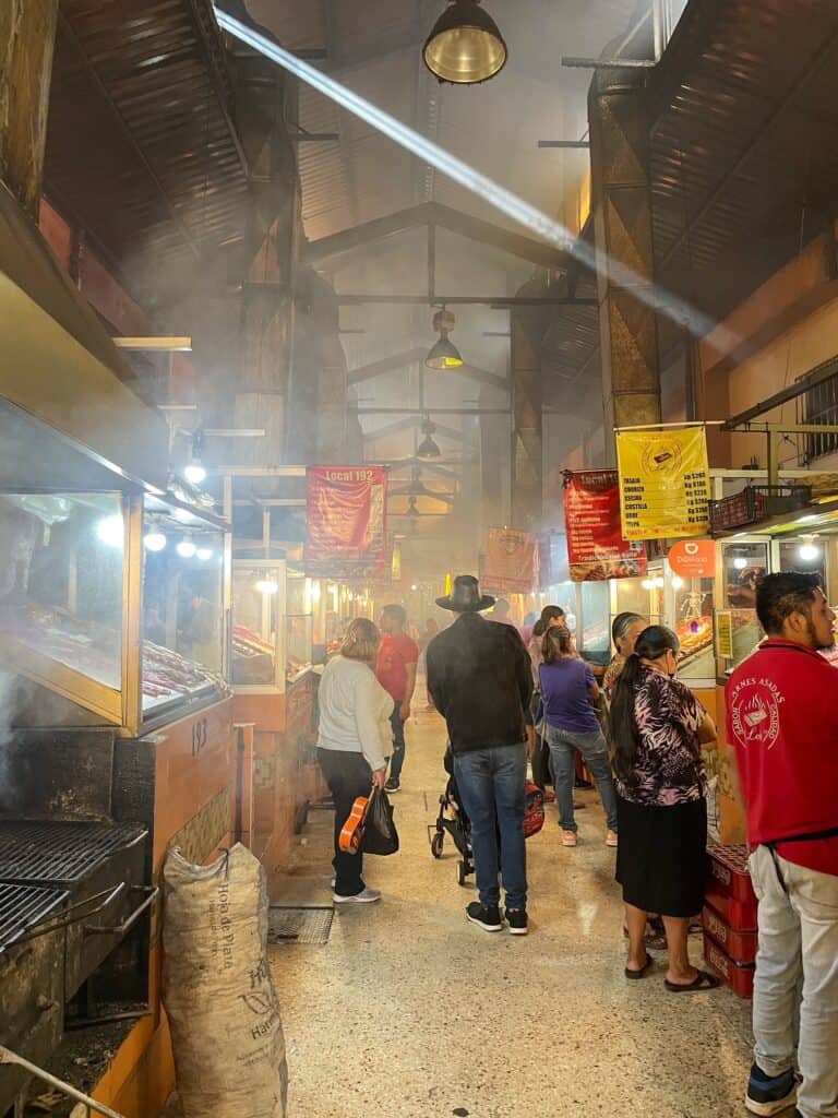 Walking through a smoky aisle where meats are grilling on a street food tour in Oaxaca.