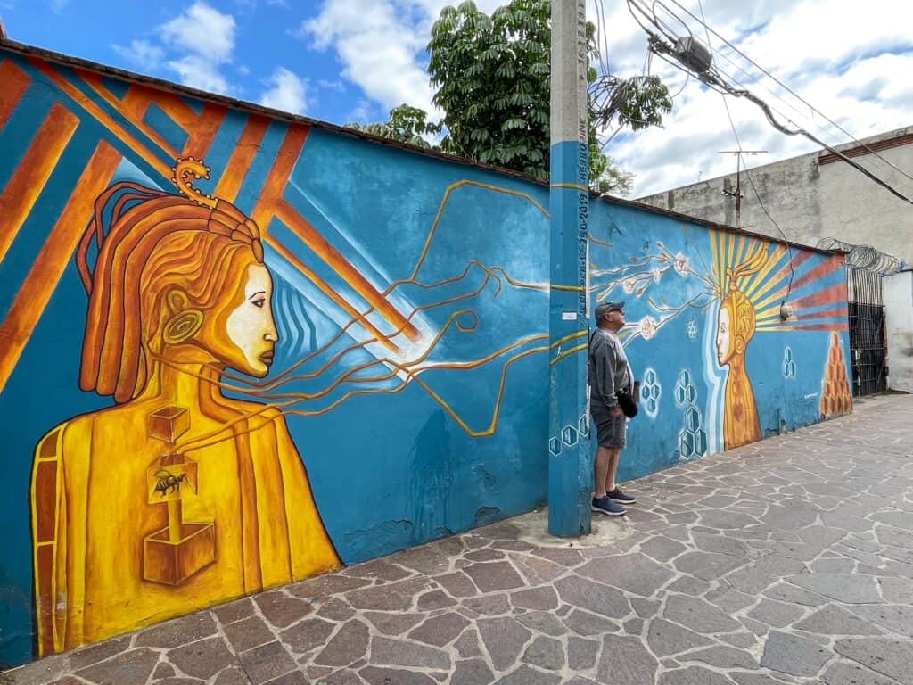 A large art mural with two indigenous people in yellow with a bright turquoise background in Xochimilco neighborhood on a art bike tour in Oaxaca.