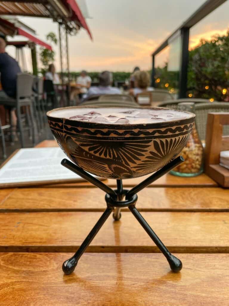 Drinking a mezcal cocktail in a unique small bowl on a tripod stand near sunset at La Azotea rooftop bar.