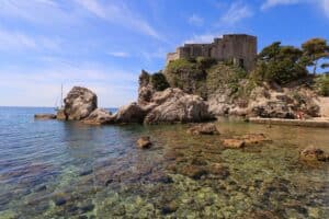A small gorgeous cove with crystal clear water and a fort up on a rocky cliff in Croatia.
