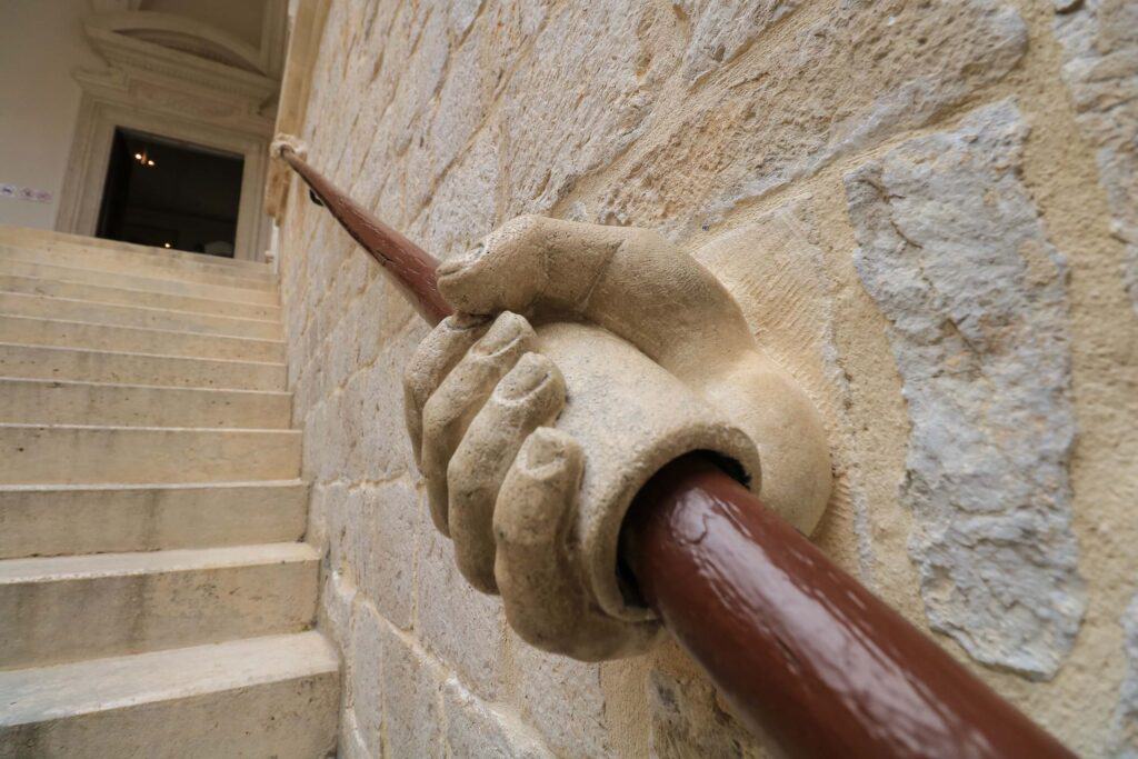 A well crafted stone hand that is holding a wooden pole as the railing of a stone staircase in the Rector's Palace in Dubrovnik, Croatia.