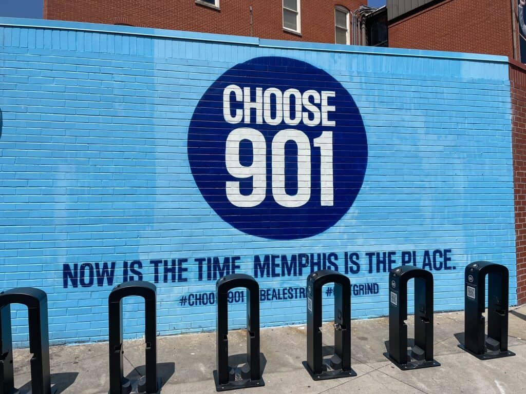 A large art mural in pale blue with a dark blue circle with "Choose 901, Memphis is the place to be" in downtown Memphis.