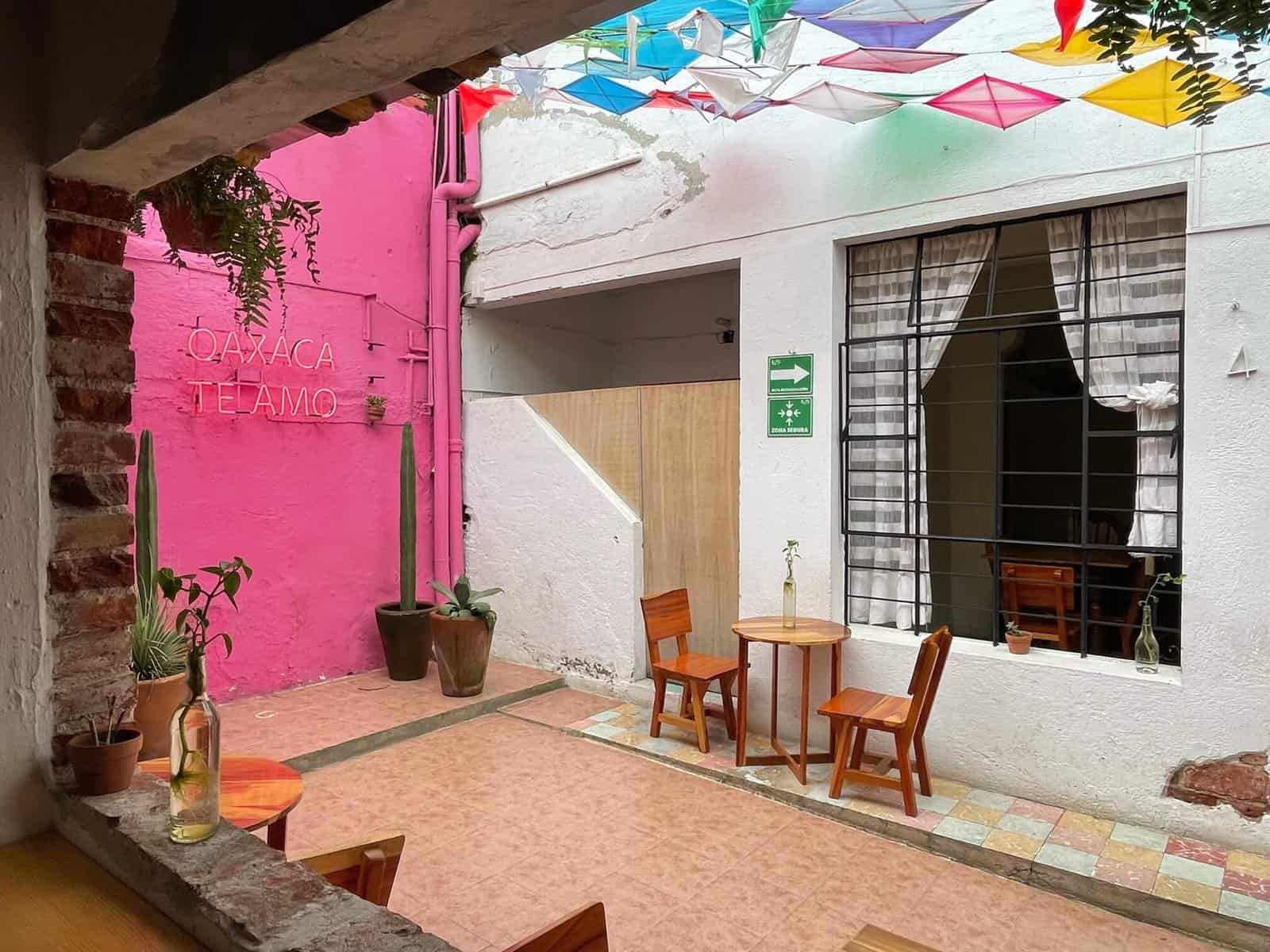 A small patio at the end of a corridor and open roof with small table and chairs, a pink wall that has a sign "Oaxaca Te Amo" in front of a coffee shop in Oaxaca.
