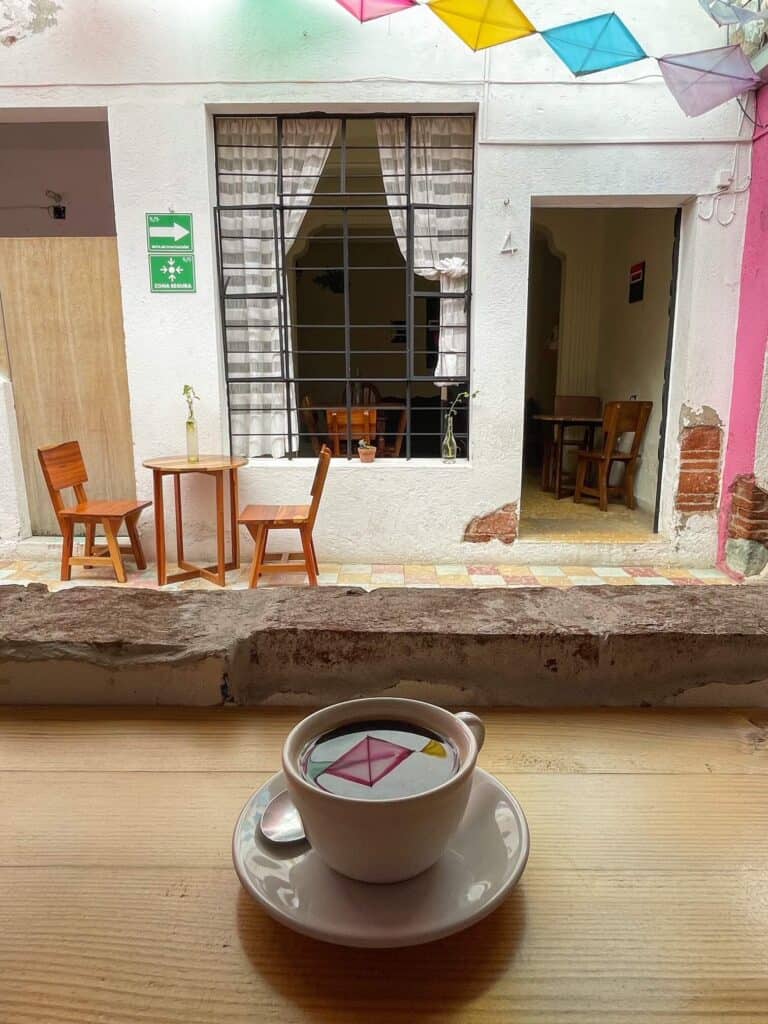 Sitting at a coffee shop in Oaxaca with a reflection of the colorful hanging squares overhead in my black coffee with a table and chairs across.