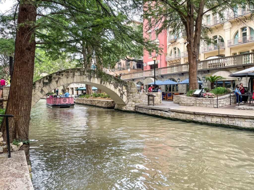 San Antonio Riverwalk lined with trees and an arched bridge.