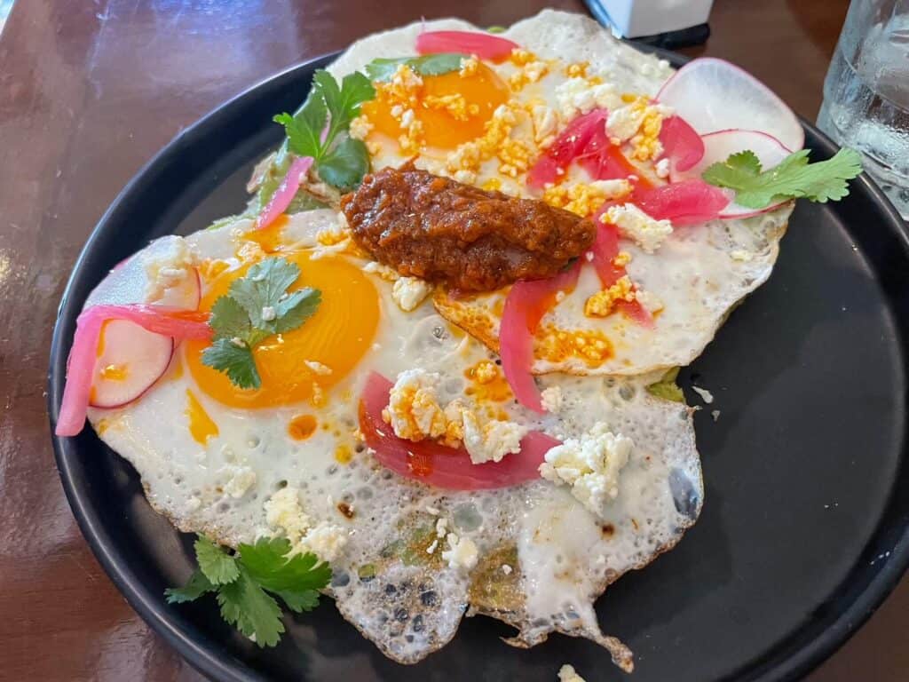 A plate with toast topped with two fried eggs, salsa, cilantro, pickled red onions, and salsa in the Yucatan Peninsula, Mexico.