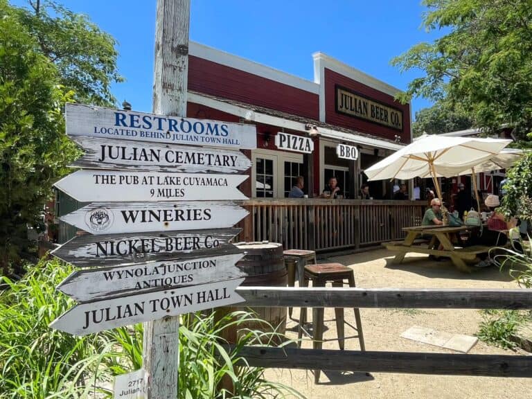 A white wooden pole with different signs for various Julian attractions pointing left or right in front of the Julian Beer Co.