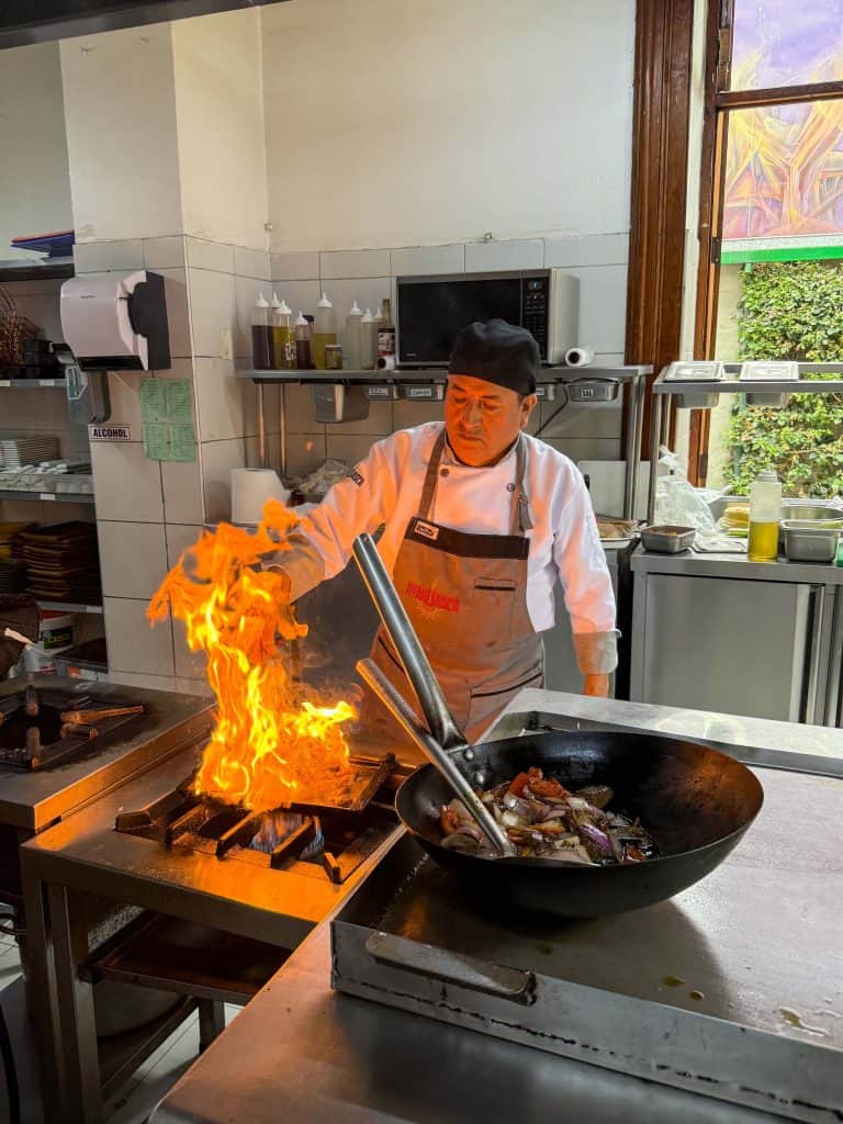 A cook making Lomo Saltado dish in a wok with high flames at a restaurant in Barranco, Lima on a food tour.