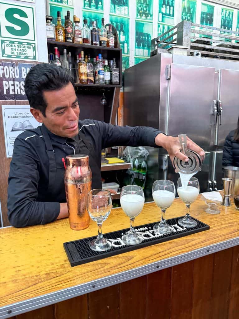 A bartender making 4 Pisco Sour drinks after shaking up all the ingredients in a shaker in Juantio Barranco, Lima.