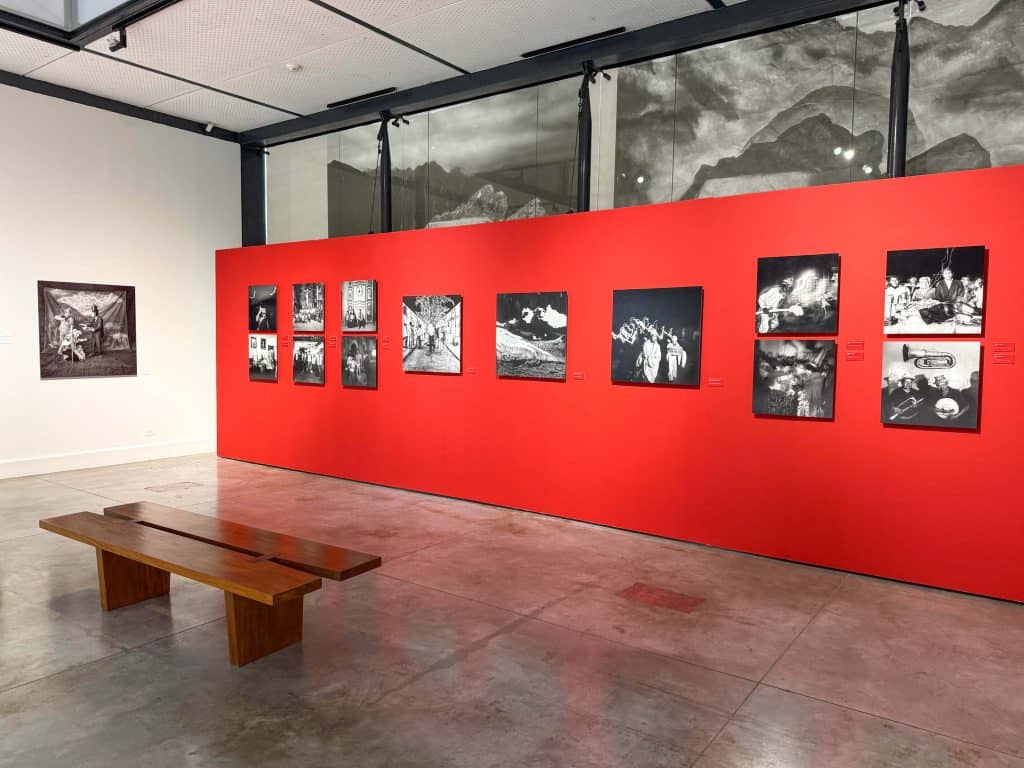 An exhibit room with one red wall and one white wall with black and white photos of Peruvian indigenous people in Peru.