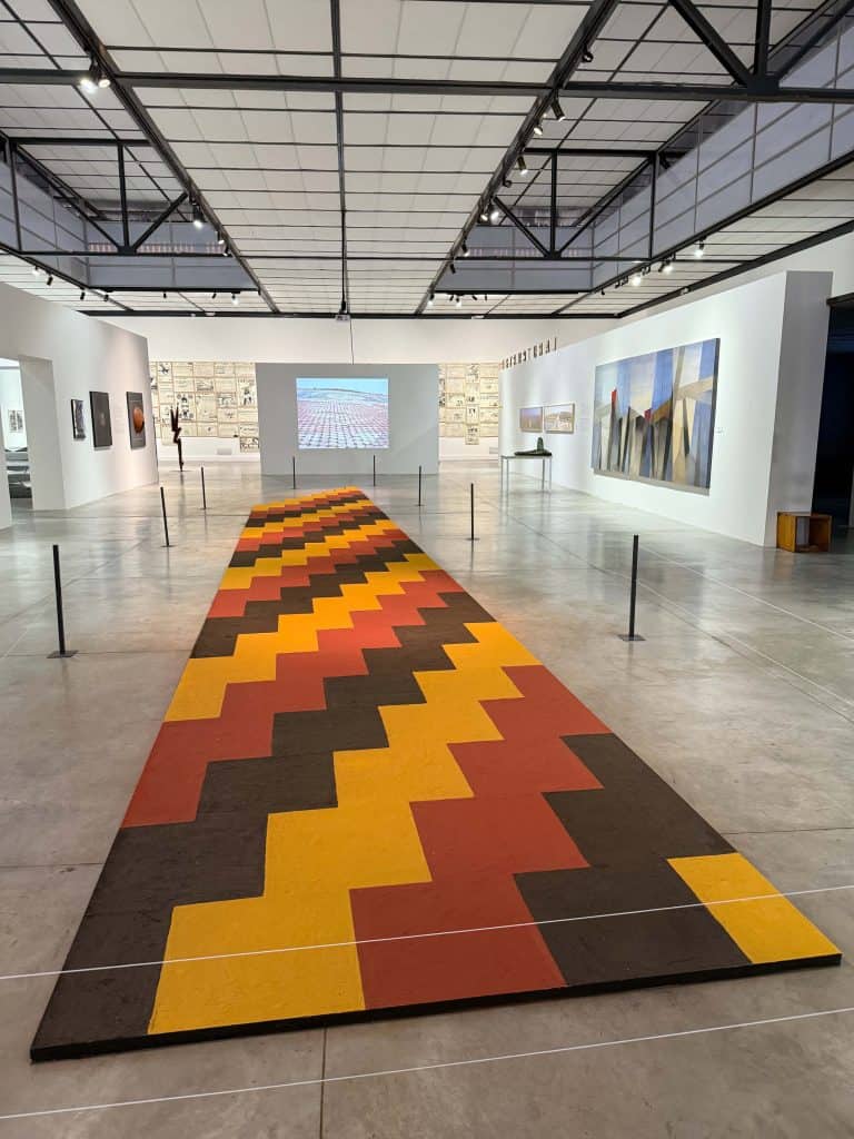 A long multi-color carpet in a large industrial space with artwork on exhibit at the MAC in Lima.