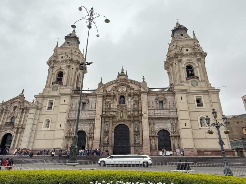 Front view of the Lima Cathedral and a long stretch SUV limousine in front on an overcast day in Lima.