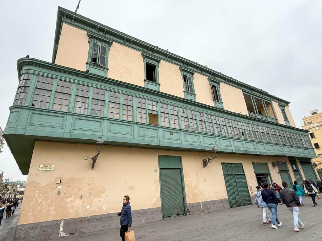 An old historic building in the historic district with pale yellow paint and a green painted wooden box balcony along the entire exterior and green trim.