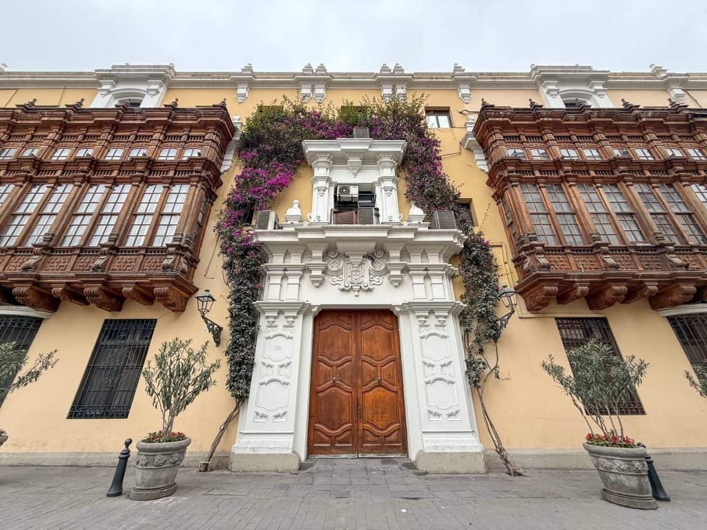 A historic yellow colored building along Plaza Mayor in Lima with wooden box balconies on the exterior.