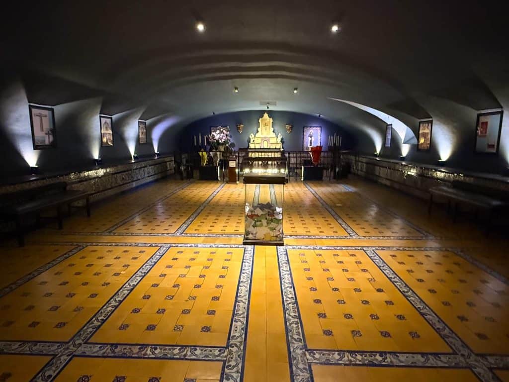 A lowly lit room at Santa Domingo Convent with yellow tiles on the floor with blue and white patterns, church relics and artifacts on the sides.