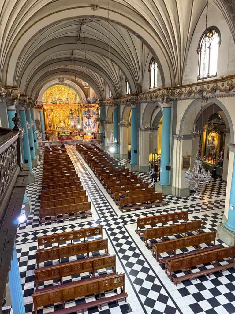 Looking down at the interior of Santo Domingo Church with its blue, white and gold colors and rows of wooden pews from the choir on the second floor