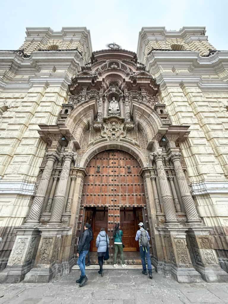 The front facade of the Church of San Francisco with large wooden doors entering the church in Lima, Peru.